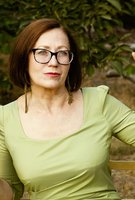 Eine Person mit Brille und grünem Oberteil sitzt im Freien vor Pflanzen und blickt zur Seite.