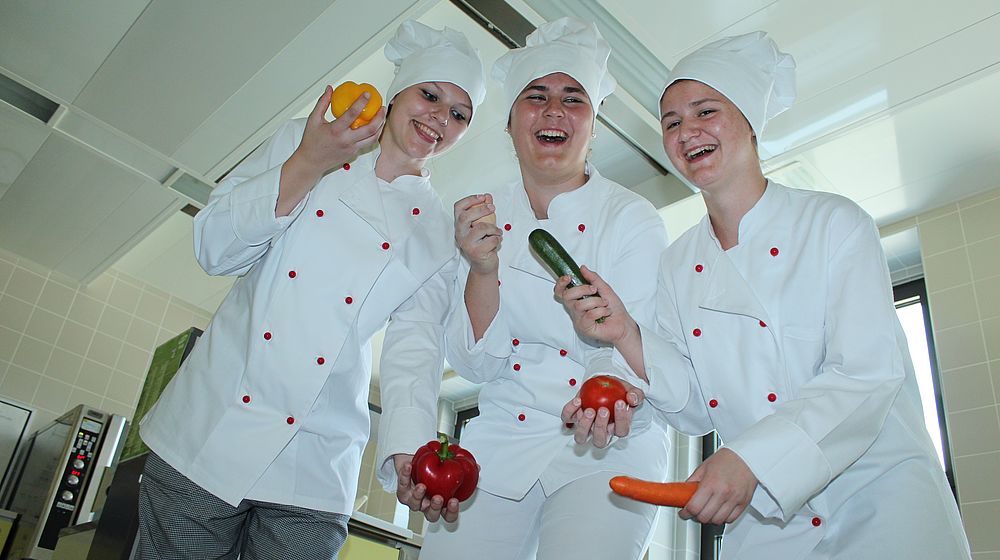 Schülerinnen halten Gemüse in den Händen während der Kochpraxis 