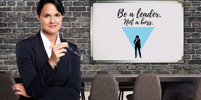 Eine weibliche Führungskraft in einem Besprechungsraum mit einer Ziegelwand, auf der Tafel steht "Be a leader not a boss".