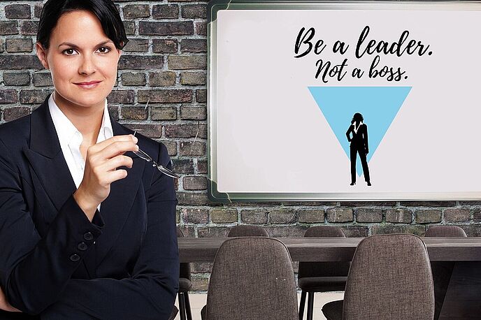 Eine weibliche Führungskraft in einem Besprechungsraum mit einer Ziegelwand, auf der Tafel steht "Be a leader not a boss".