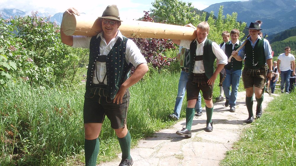 Schüler in Trachtenkleidung tragen gemeinsam Holzstamm