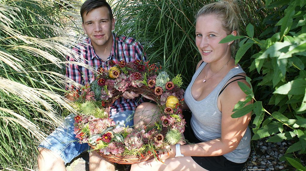 Schüler und Schülerin präsentieren Blumenkranz