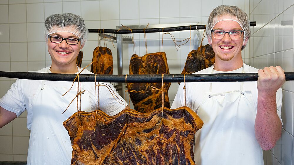 Zwei Schüler halten eine Stange auf der ein Stück Fleisch hängt