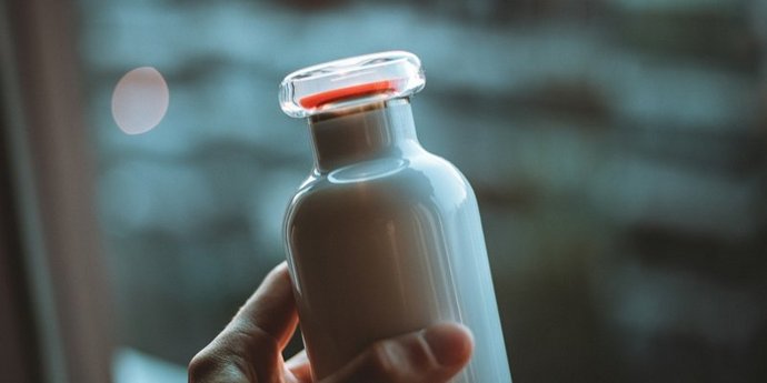 nicolas-j-leclercq-6tRPm5tLnY4-unsplash - ©Nicolas J. Leclercq Hand hält Glasflasche voller Milch mit Glasverschluss.