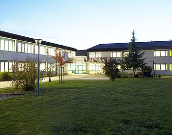 Rasenfläche mit Schulgebäude von außen