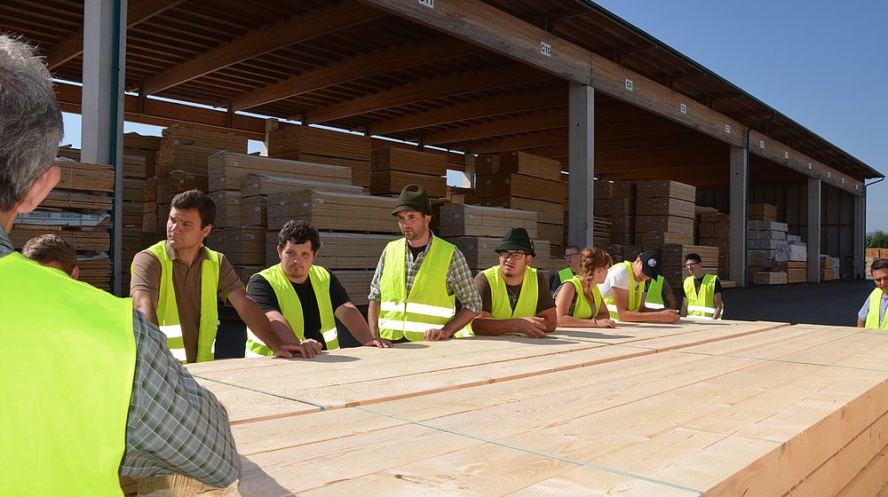 Schülerinnen und Schüler stehen um einen Stoß geschnittenes Holz