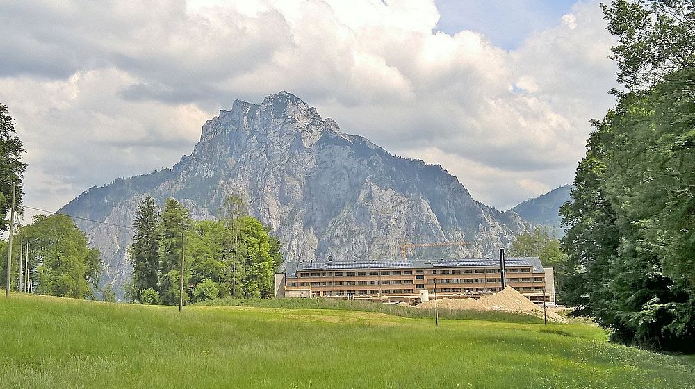 Schulgebäude mit Wiese im Vordergrund und Berg im Hintergrund