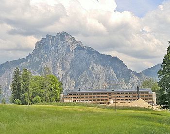 Schulgebäude mit Wiese im Vordergrund und Berg im Hintergrund