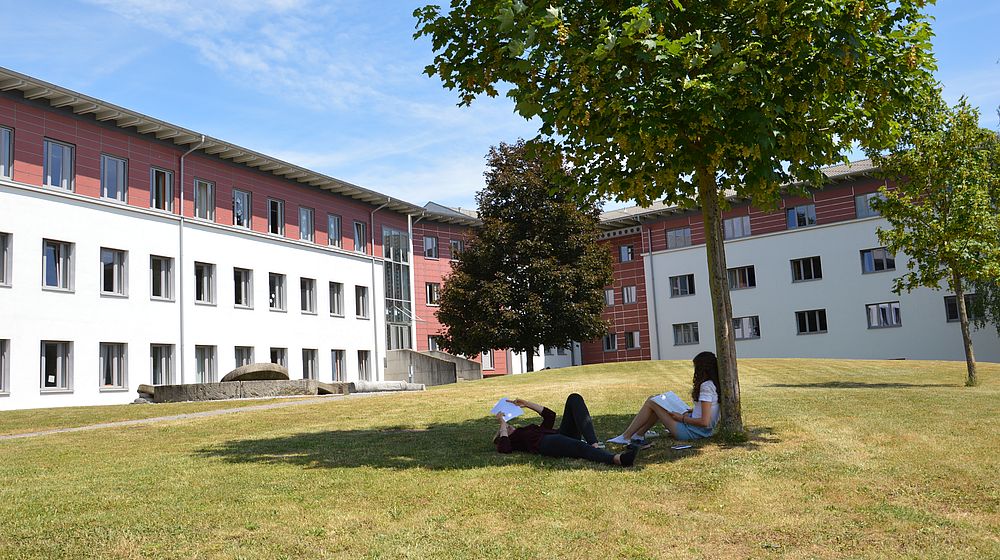 Schülerinnen sitzen unter einem Baum, im Hintergrund befindet sich das Schulgebäude