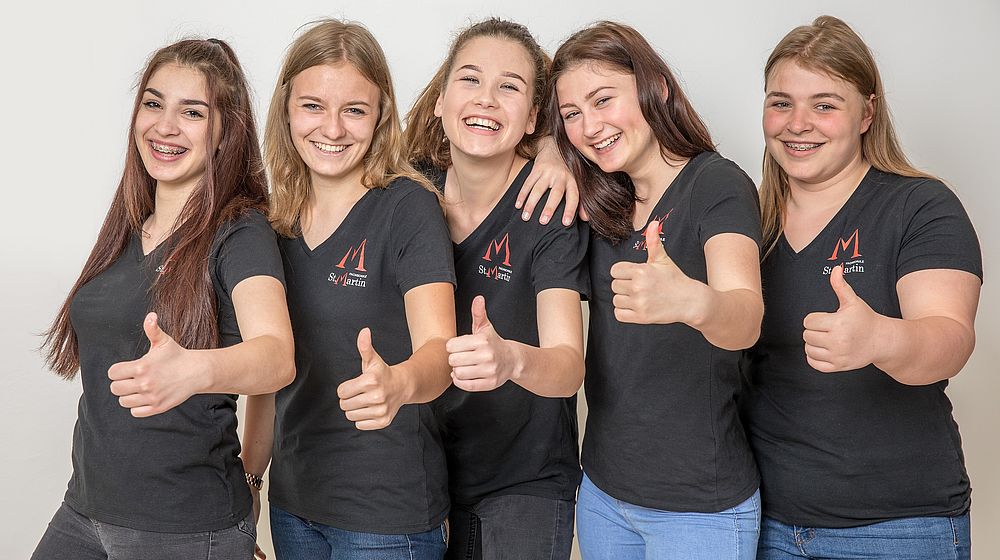 5 Schülerinnen zeigen Daumen im Schullogo T-Shirt